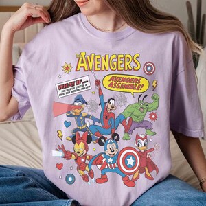 May include: A lilac t-shirt with a comic-style illustration of The Avengers characters, including Mickey Mouse as Captain America, Spider-Man, and Donald Duck. The text "The Avengers" and "Avengers Assemble!" are also displayed.