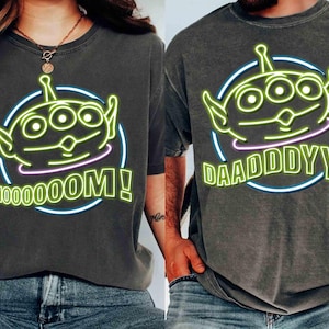 May include: Two gray t-shirts with a green alien character graphic. One shirt says "Mooooom!" and the other says "Daadddyy!"