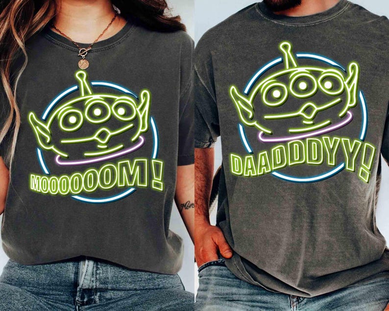 May include: Two gray t-shirts with a green alien character graphic. One shirt says "Mooooom!" and the other says "Daadddyy!"