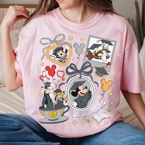 Puede incluir: Una camiseta rosa claro con personajes de Disney celebrando la graduaci&oacute;n. Mickey Mouse, el Pato Donald y Goofy se muestran con atuendos de graduaci&oacute;n dentro de marcos e ilustraciones, junto con gorras de graduaci&oacute;n, globos y estrellas. La camiseta tiene cuello redondo y mangas cortas.
