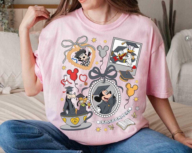 Puede incluir: Una camiseta rosa claro con personajes de Disney celebrando la graduaci&oacute;n. Mickey Mouse, el Pato Donald y Goofy se muestran con atuendos de graduaci&oacute;n dentro de marcos e ilustraciones, junto con gorras de graduaci&oacute;n, globos y estrellas. La camiseta tiene cuello redondo y mangas cortas.