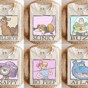 May include: Six cream-colored t-shirts, each featuring a different cartoon character in a framed design. Characters include Bullseye, Slinky, Buzz, Snappy, Bo Peep, and Atlas. Each shirt has the character's name printed below the image.