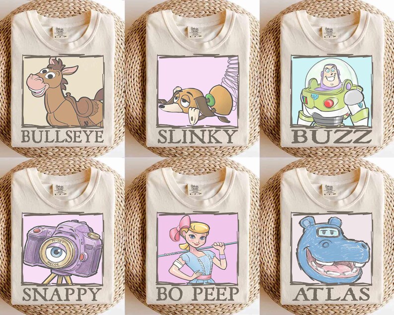 May include: Six cream-colored t-shirts, each featuring a different cartoon character in a framed design. Characters include Bullseye, Slinky, Buzz, Snappy, Bo Peep, and Atlas. Each shirt has the character's name printed below the image.