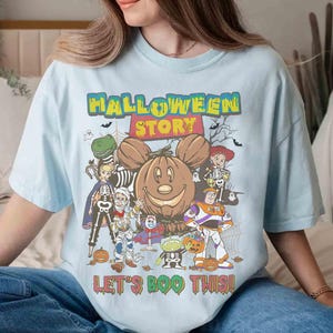 Puede incluir: Camiseta azul claro con un dise&ntilde;o tem&aacute;tico de Halloween. El dise&ntilde;o presenta un Mickey Mouse con forma de calabaza, personajes de dibujos animados con disfraces de Halloween y el texto "HALLOWEEN STORY" y "LET'S BOO THIS!"