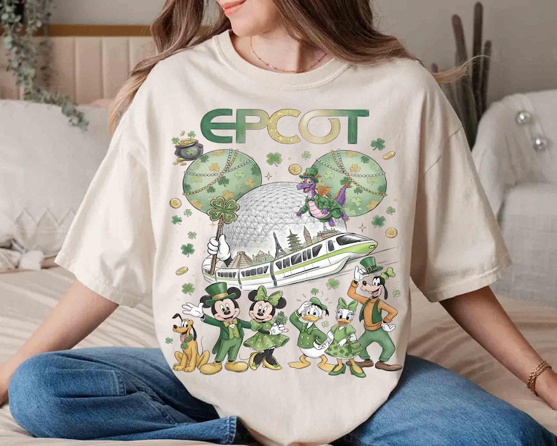 May include: Cream-coloured t-shirt with a St. Patrick's Day EPCOT design. The graphic features Mickey and Minnie Mouse, Donald and Daisy Duck, Goofy, and Pluto in green outfits, a monorail, and the EPCOT sphere.