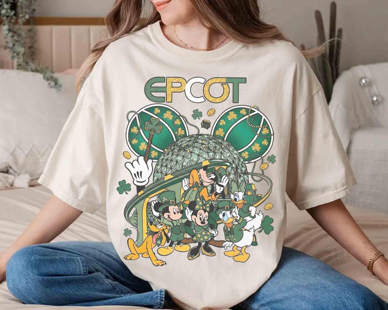May include: Cream-colored t-shirt featuring a graphic of Disney characters dressed in green for St. Patrick's Day. The design includes Mickey and Minnie Mouse, Donald and Daisy Duck, and Pluto, with the word "EPCOT" above.