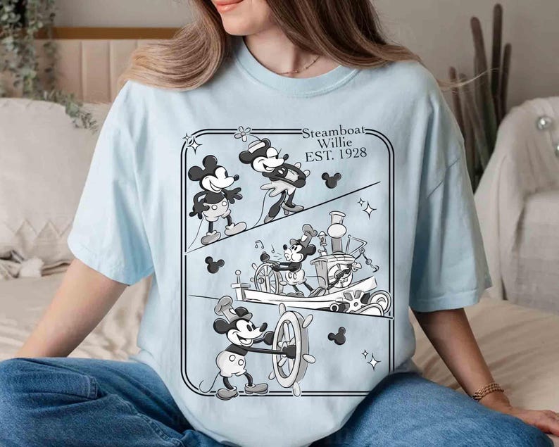Może przedstawiać: Jasnoniebieska koszulka z czarno-białą grafiką Myszki Miki ze Steamboat Willie. Grafika przedstawia Myszkę Miki w r&oacute;żnych scenach z filmu z 1928 roku, z napisem "Steamboat Willie EST. 1928".