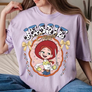 May include: Purple t-shirt with a cartoon image of Jessie from Toy Story. The shirt has the text "Jessie Cowgirl" in a colorful font.