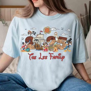 May include: Pale blue t-shirt with a vibrant graphic design incorporating the number "25" and cartoon characters like Mickey Mouse and Donald Duck. The words "The Lee Family" are printed beneath the design.