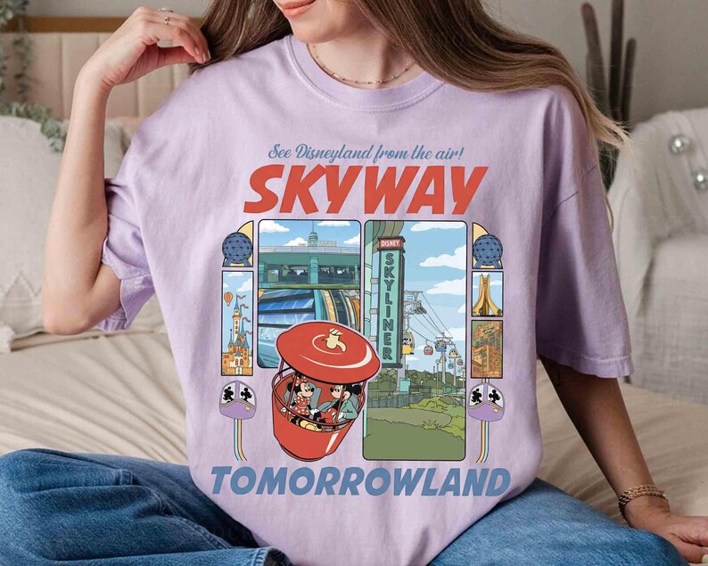Puede incluir: Una camiseta lila con un gr&aacute;fico del paseo Skyway de Disneyland. El dise&ntilde;o incluye las palabras "SKYWAY" y "TOMORROWLAND", junto con ilustraciones del paseo e iconos del parque. La camiseta es de corte holgado.