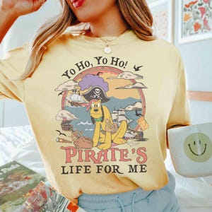 May include: Yellow t-shirt with a pirate-themed graphic featuring a cartoon dog, pirate ship, and the text "Yo Ho, Yo Ho! Pirate's Life For Me." The design is set within a circular frame.