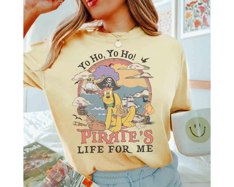 May include: Yellow t-shirt with a pirate-themed graphic featuring a cartoon dog, pirate ship, and the text "Yo Ho, Yo Ho! Pirate's Life For Me." The design is set within a circular frame.