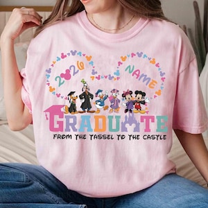 Może przedstawiać: Jasnor&oacute;żowa koszulka z postaciami Disneya, w tym Myszka Miki i Myszka Minnie, Goofy i Kaczor Donald. Koszulka zawiera napis "2026 NAME GRADUATE FROM THE YASSEL TO THE CASTLE" w r&oacute;żnych kolorach i wzorach.