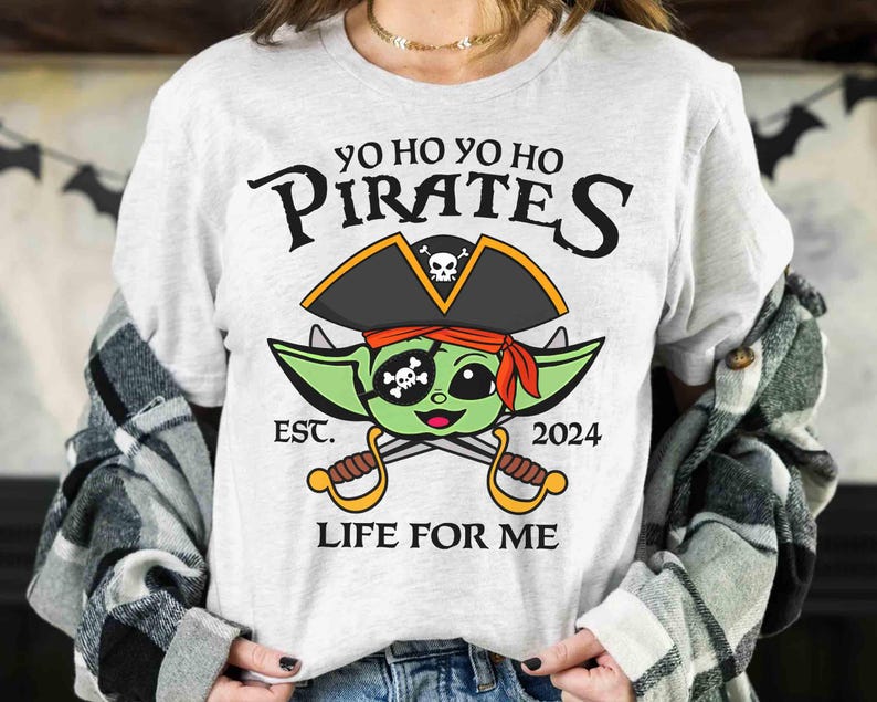 May include: A white t-shirt with a green alien wearing a pirate hat and holding crossed swords. The text on the shirt reads "Yo Ho Yo Ho Pirates Est. 2024 Life For Me".