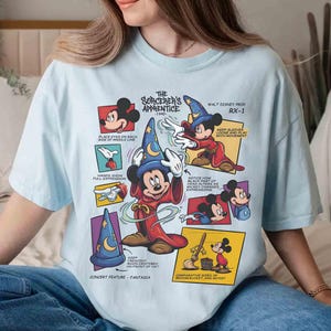 May include: Light blue t-shirt featuring a graphic of Mickey Mouse as the Sorcerer's Apprentice from Fantasia. The design includes text and illustrations from the 1940 Walt Disney production, RX-1. The shirt has short sleeves and a crew neck.