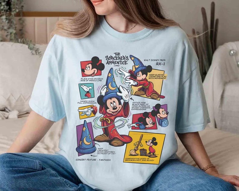 May include: Light blue t-shirt featuring a graphic of Mickey Mouse as the Sorcerer's Apprentice from Fantasia. The design includes text and illustrations from the 1940 Walt Disney production, RX-1. The shirt has short sleeves and a crew neck.
