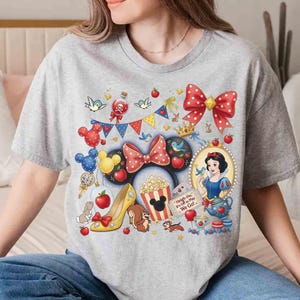 May include: A gray t-shirt featuring a colorful graphic design with Disney-themed elements. The design includes a red polka-dot bow, Snow White, Mickey Mouse ears, popcorn, and the text "Heigh-Ho, It's Off to Play We Go!"