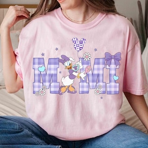 Puede incluir: Camiseta rosa claro con la palabra "MIMI" en un dise&ntilde;o de cuadros vichy morado, con Daisy Duck sosteniendo un globo. El dise&ntilde;o incluye estrellas, corazones y flores, creando una est&eacute;tica caprichosa y alegre.