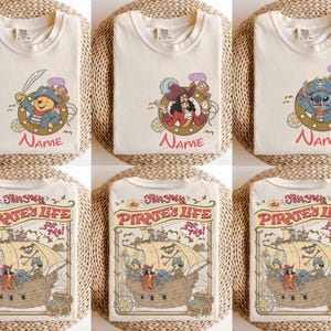 K&ouml;nnte beinhalten: Cremefarbene T-Shirts mit verschiedenen Piraten-Cartoon-Designs. Ein Shirt zeigt Winnie Puuh, ein anderes Captain Hook und ein drittes Stitch. Die unteren Shirts zeigen ein Piratenschiff mit dem Text "Pirate's Life for Me!"