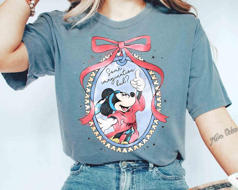 May include: A blue t-shirt with a Mickey Mouse cartoon design. Mickey is in a red outfit, giving a thumbs-up within an oval frame, a pink bow, and the text "Some imagination huh?"
