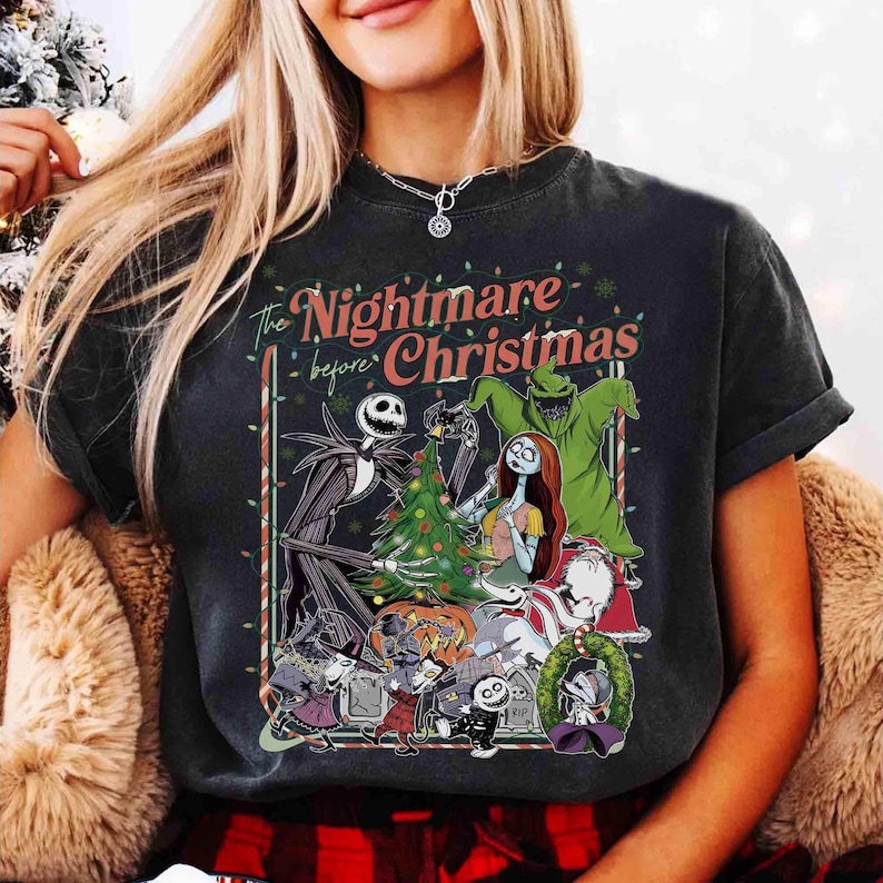 K&ouml;nnte beinhalten: Dunkelgraues T-Shirt mit einer Grafik aus "The Nightmare Before Christmas". Das Design zeigt Jack Skellington, Sally und andere Charaktere um einen Weihnachtsbaum. Der Text "The Nightmare Before Christmas" ist in Rot und Wei&szlig;.