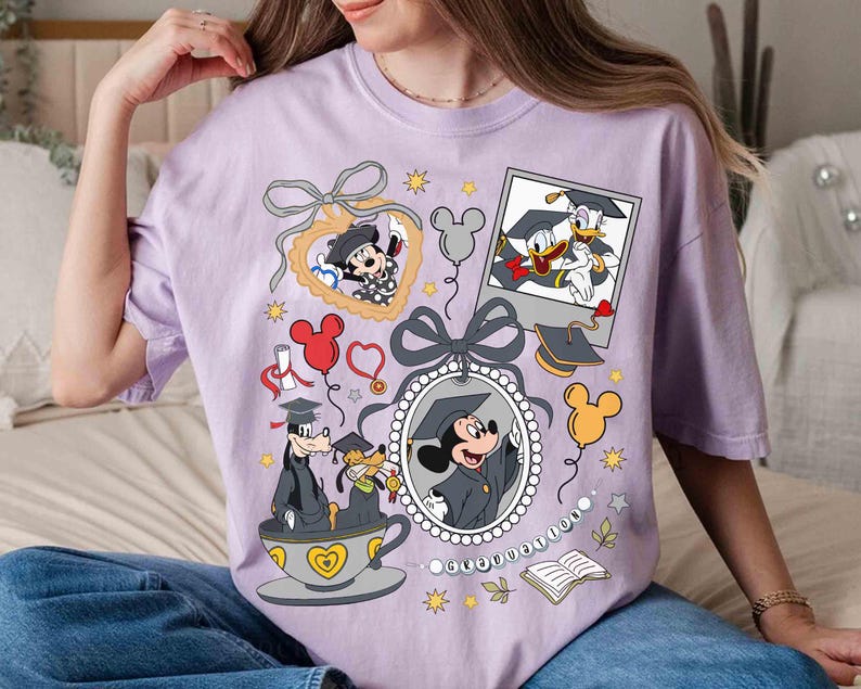 Puede incluir: Una camiseta lila claro con gr&aacute;ficos de Disney con tem&aacute;tica de graduaci&oacute;n. Mickey Mouse, Donald Duck y Goofy est&aacute;n representados con atuendos de graduaci&oacute;n. El dise&ntilde;o incluye globos, diplomas y una taza de t&eacute; con corazones.