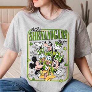 May include: A gray t-shirt featuring a St. Patrick's Day design with Mickey Mouse, Minnie Mouse, Donald Duck, Daisy Duck, Goofy, and Pluto. The text "Let The Shenanigans Begin" is in a green frame with shamrocks.