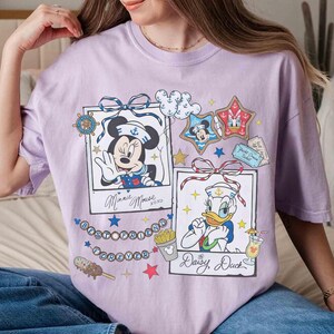 May include: A light purple t-shirt featuring two framed illustrations of Disney characters Minnie Mouse and Daisy Duck. The shirt includes the text "Best Friends Forever" and other nautical-themed graphics.