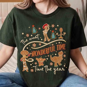 Puede incluir: Camiseta verde oscuro con un dise&ntilde;o festivo. El texto dice "the most WONDERFUL TIME Time the year". El dise&ntilde;o incluye personajes de dibujos animados, copos de nieve y &aacute;rboles de Navidad. Una camiseta navide&ntilde;a divertida y caprichosa.