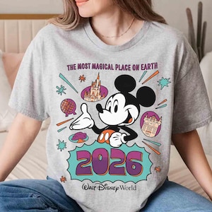 May include: A grey t-shirt with a Mickey Mouse design, the text reads "THE MOST MAGICAL PLACE ON EARTH" and "2026 Walt Disney World". The design includes Disney landmarks and colourful accents.