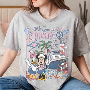 Peut inclure: T-shirt gris avec l'inscription "Girls Gone Cruising" et un motif de bateau de croisi&egrave;re, phare, palmiers et personnages de dessins anim&eacute;s. Minnie et Daisy Duck font le signe de la paix.