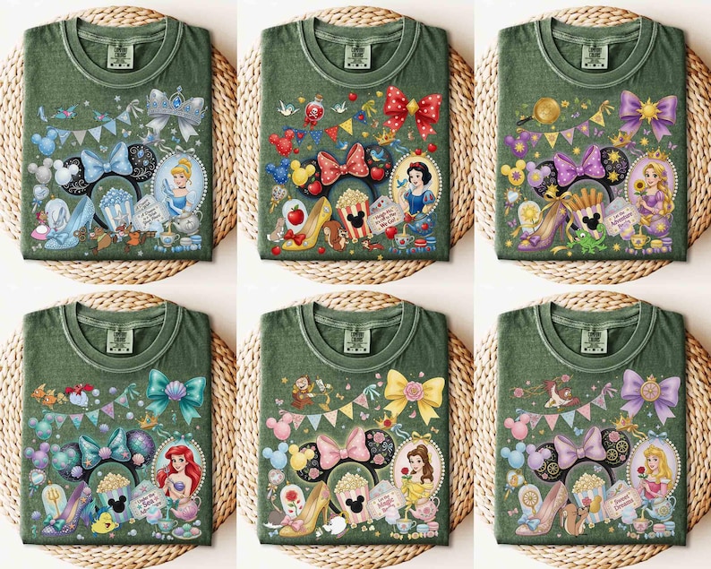 May include: Six olive green t-shirts with colorful Disney princess-themed designs. Each shirt features a different princess, such as Cinderella, Snow White, and Ariel, along with related imagery like bows, shoes, and teacups. The shirts are displayed on a woven surface.