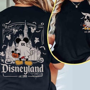 May include: Black t-shirt with a Disneyland Halloween design. The graphic shows Mickey Mouse as a ghost with a pumpkin, a castle, and the text "Disneyland est. 1955". The design also includes bats and Mickey Mouse balloons.