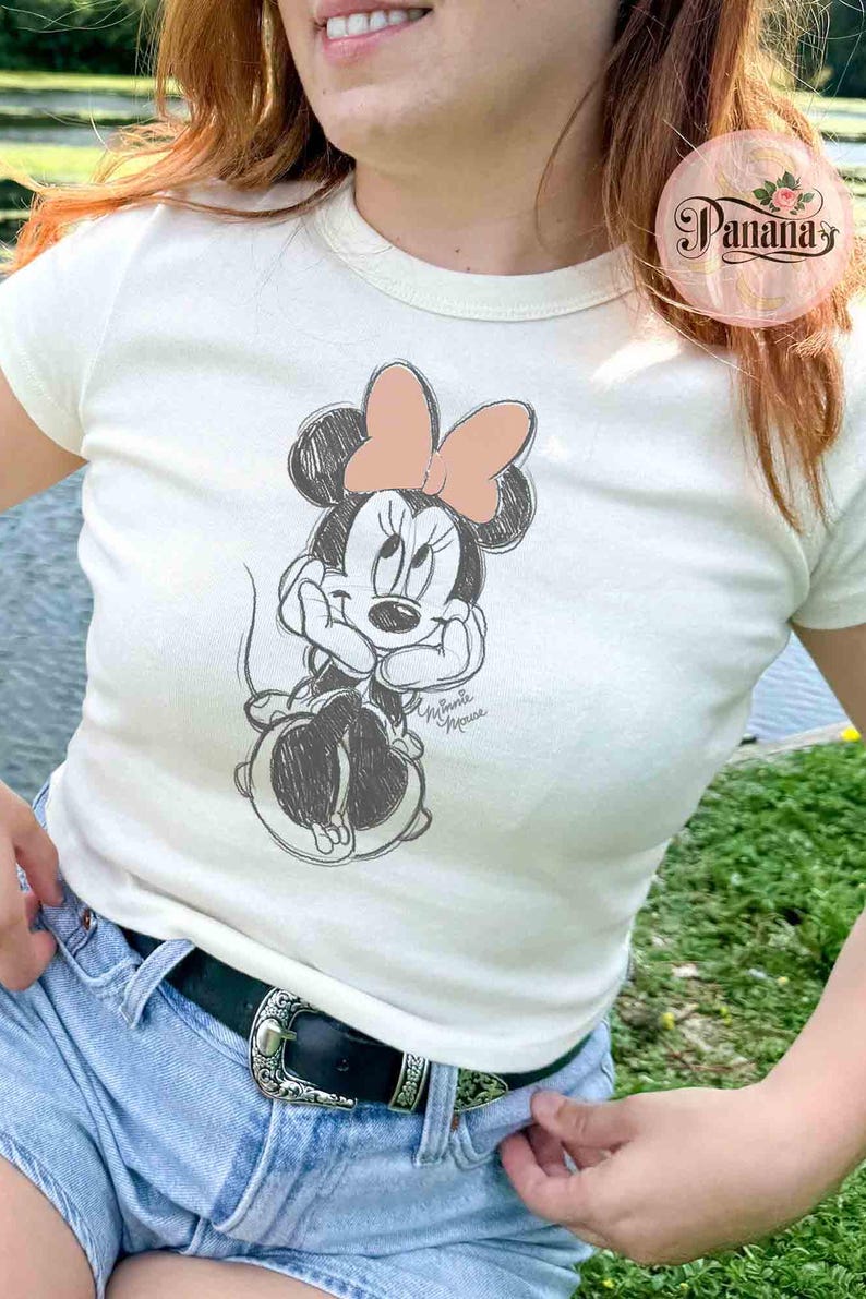 May include: A white t-shirt with a sketch of Minnie Mouse wearing a pink bow. The text "Minnie Mouse" is written below the image.