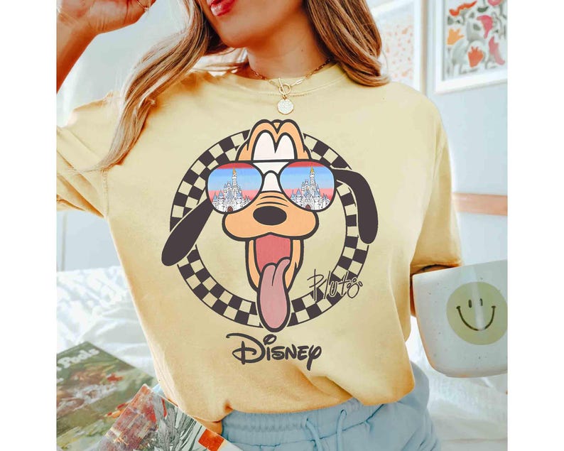 May include: A yellow t-shirt with a cartoon image of Pluto wearing sunglasses. The sunglasses reflect an image of Cinderella's castle. The text "Pluto" and "Disney" are printed on the shirt.