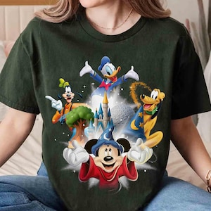 May include: Dark green t-shirt featuring a colorful graphic of Disney characters including Mickey Mouse, Donald Duck, Goofy, and Pluto. The design includes a castle and other iconic elements from Disney films. The shirt is a comfortable, casual style.