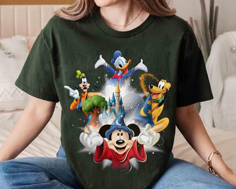 May include: Dark green t-shirt featuring a colorful graphic of Disney characters including Mickey Mouse, Donald Duck, Goofy, and Pluto. The design includes a castle and other iconic elements from Disney films. The shirt is a comfortable, casual style.