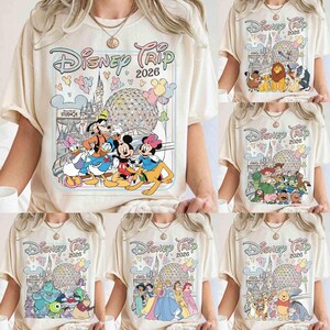 May include: Cream-colored t-shirts with various Disney character graphics. Each shirt features the text "Disney Trip 2026" in a whimsical font, along with iconic Disney imagery like Mickey Mouse, princesses, and other characters.