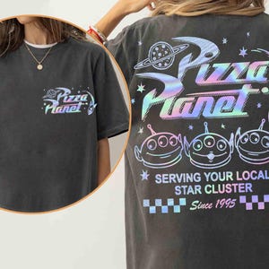 May include: Dark gray t-shirt with a Pizza Planet logo on the front and back. The back features the Pizza Planet logo, three alien characters, and the text "Serving Your Local Star Cluster Since 1995" in a holographic design.