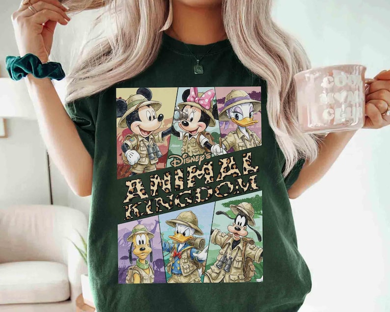 K&ouml;nnte beinhalten: Dunkelgr&uuml;nes T-Shirt mit einer Grafik der Disney-Figuren Mickey Mouse, Minnie Mouse, Donald Duck, Daisy Duck, Goofy und Pluto in Safari-Outfits. Der Text "Disney's Animal Kingdom" ist ebenfalls abgebildet.