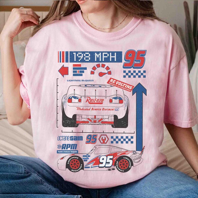 K&ouml;nnte beinhalten: Ein hellrosa T-Shirt mit einem Grafikdruck des Rennwagens Lightning McQueen. Das Design enth&auml;lt den Text 198 MPH, 95, Rust-eze, Medicated Bumper Ointment, Re-Volting, Octane Gain und RPM sowie verschiedene Rennsport-Symbole und grafische Elemente.