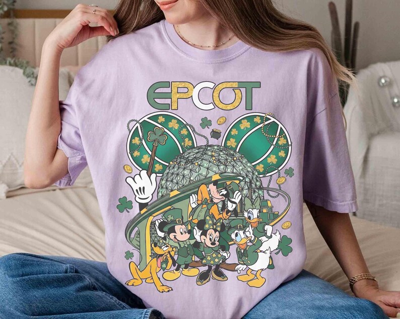 May include: A light purple t-shirt featuring the word "EPCOT" in green and gold lettering. The graphic includes Mickey Mouse, Minnie Mouse, Donald Duck, and Pluto in St. Patrick's Day attire, with shamrocks and a stylized Spaceship Earth.