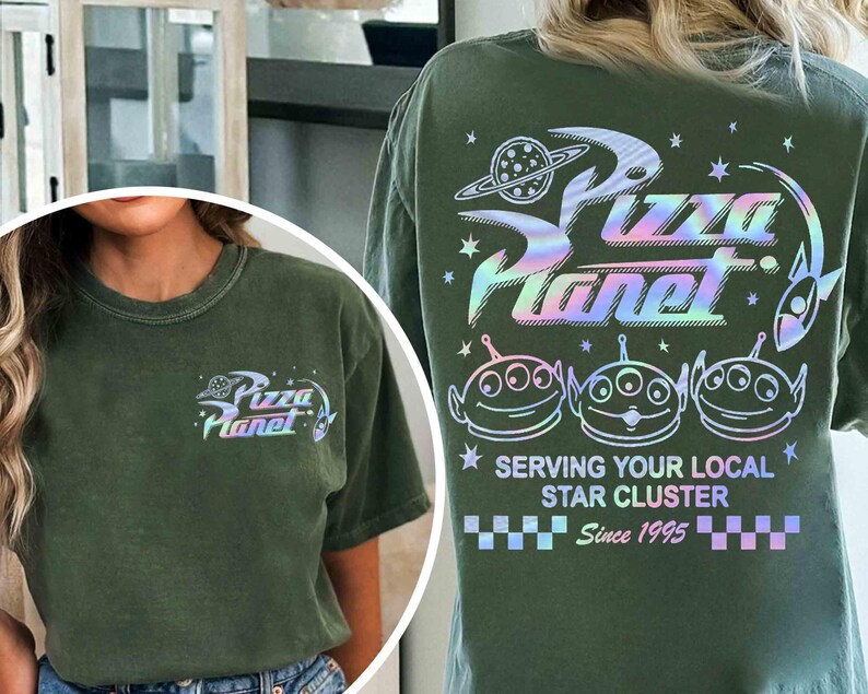 May include: Olive green t-shirt featuring the Pizza Planet logo with a holographic design on the front and back. The back of the shirt displays the Pizza Planet logo, three alien characters, and the text "Serving Your Local Star Cluster Since 1995."