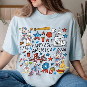 Puede incluir: Camiseta azul claro con un gr&aacute;fico colorido que celebra el 250 aniversario de Am&eacute;rica. El dise&ntilde;o incluye personajes de dibujos animados, el Capitolio, un bate de b&eacute;isbol, estrellas y el texto "1776 HAPPY 250 AMERICA 2026".