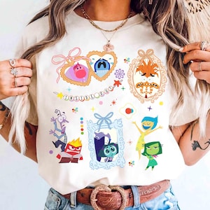 Peut inclure: T-shirt crème avec un motif coloré des personnages du film "Vice-Versa". Le design comprend des portraits encadrés de personnages comme Joie, Tristesse et Colère, ainsi que le texte "Inside Out".