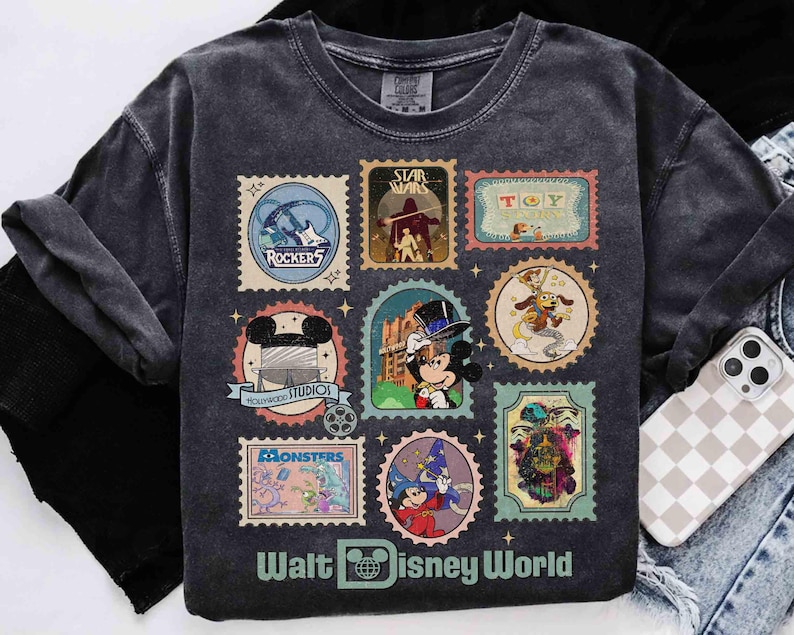Puede incluir: Camiseta gris oscuro con dise&ntilde;os de sellos postales tem&aacute;ticos de Disney. Los sellos incluyen im&aacute;genes de Rockers, Star Wars, Toy Story, Mickey Mouse, Monsters y m&aacute;s. Las palabras "Walt Disney World" est&aacute;n impresas en la parte inferior.