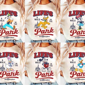 May include: Cream-colored sweatshirts featuring various Disney characters like Goofy, Pluto, Minnie Mouse, Daisy Duck, Mickey Mouse, and Donald Duck. Each shirt has the text "Life's a Walk in the Park" with the Walt Disney World logo.