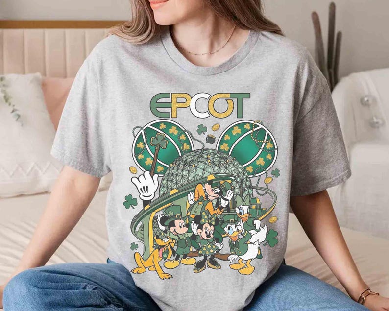 May include: A gray t-shirt featuring the word "EPCOT" in gold lettering. The shirt has a graphic of Disney characters dressed in green, with shamrocks and the EPCOT ball. The characters include Mickey, Minnie, Donald, Goofy, and Pluto.