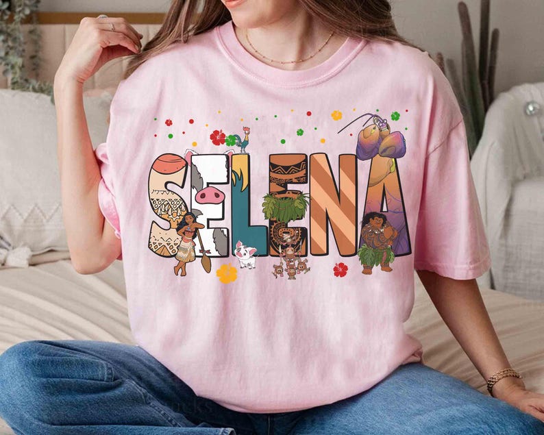 Puede incluir: Camiseta rosa claro con el nombre "Selena" en letras decorativas y coloridas. Cada letra est&aacute; dise&ntilde;ada con un patr&oacute;n y personaje diferente de una pel&iacute;cula de animaci&oacute;n popular. La camiseta es de estilo casual y c&oacute;modo.