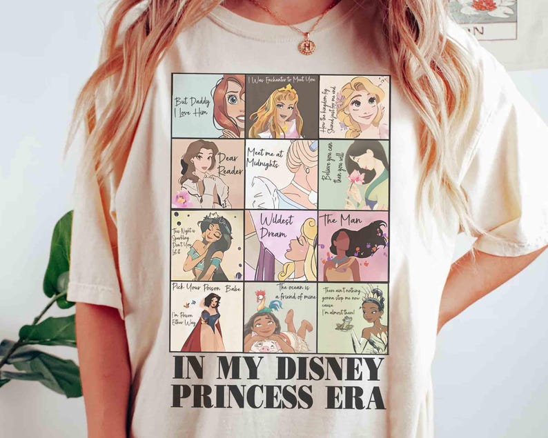 May include: Cream-colored t-shirt featuring a grid of Disney princess illustrations with quotes. The shirt includes the text "IN MY DISNEY PRINCESS ERA" in a bold, black font. The design showcases various princesses in colorful squares.